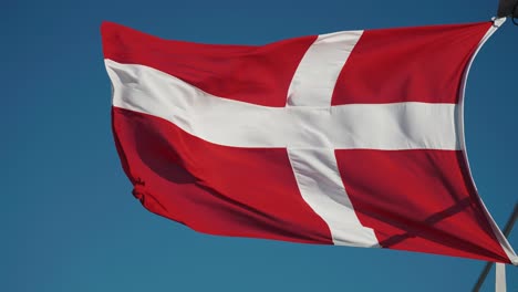 danish flag flutters in the wind against the blue cloudless sky