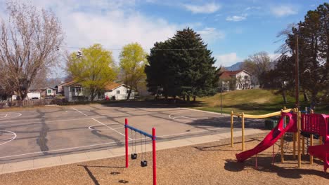 drone flying over little park playground and basketball court revealing shoes hanging on telephone wire, and empty park playground and court on sunny spring summer day