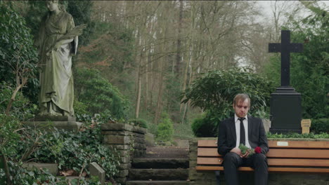 Sad-man-sitting-on-bench-in-cemetery,-medium-shot