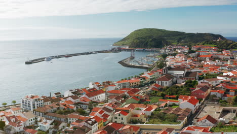 Filmische-Drohnenaufnahme-Aus-Der-Luft-Der-Malerischen-Stadt-Horta-Auf-Der-Insel-Faial,-Azoren-–-Portugal.-Hohe-Sicht-Auf-Die-Am-Hafen-Angedockten-Schiffe,-Grüne-Landschaft-Im-Hintergrund