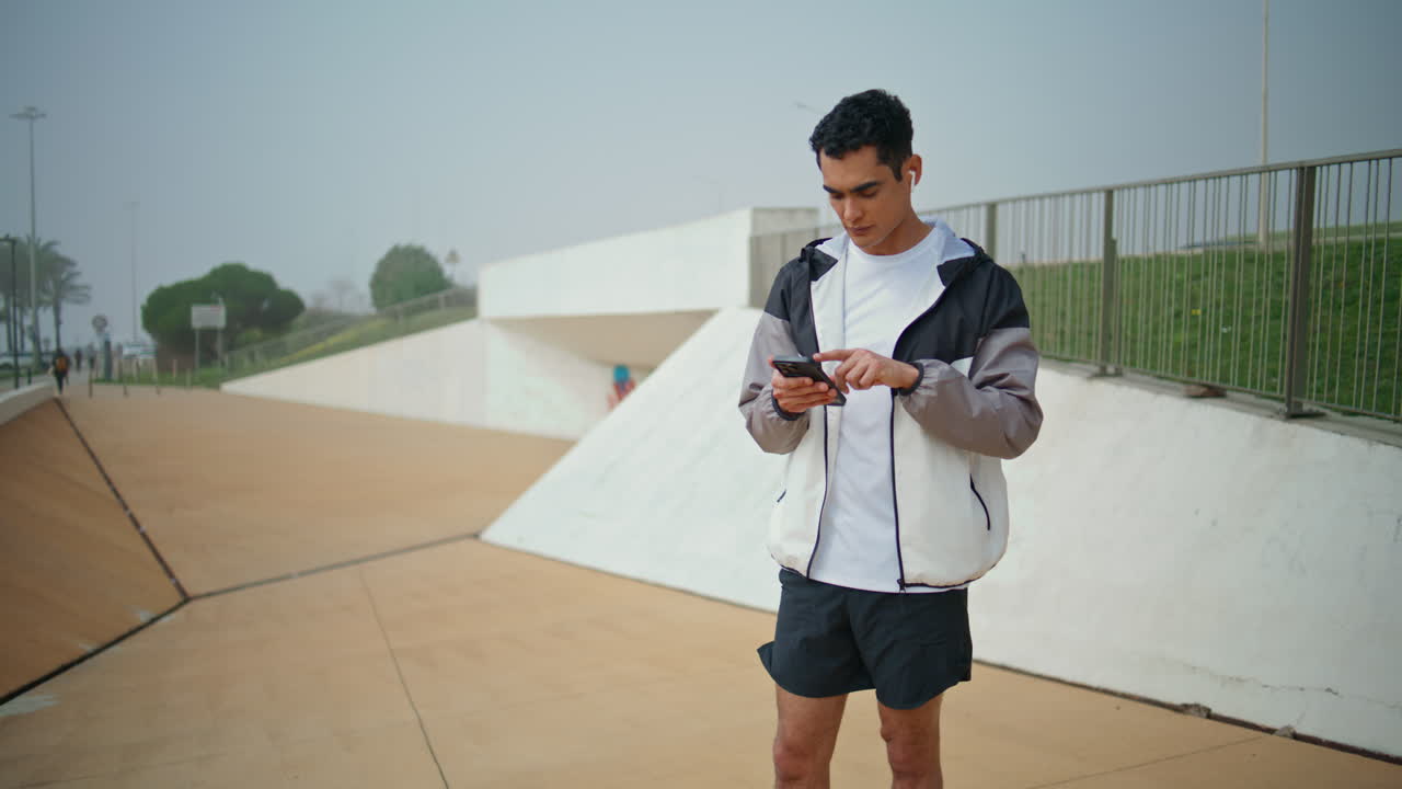 공원에서 이어폰을 착용한 운동선수. 음악을 듣고 선택하는 활동적인 건강한 남자