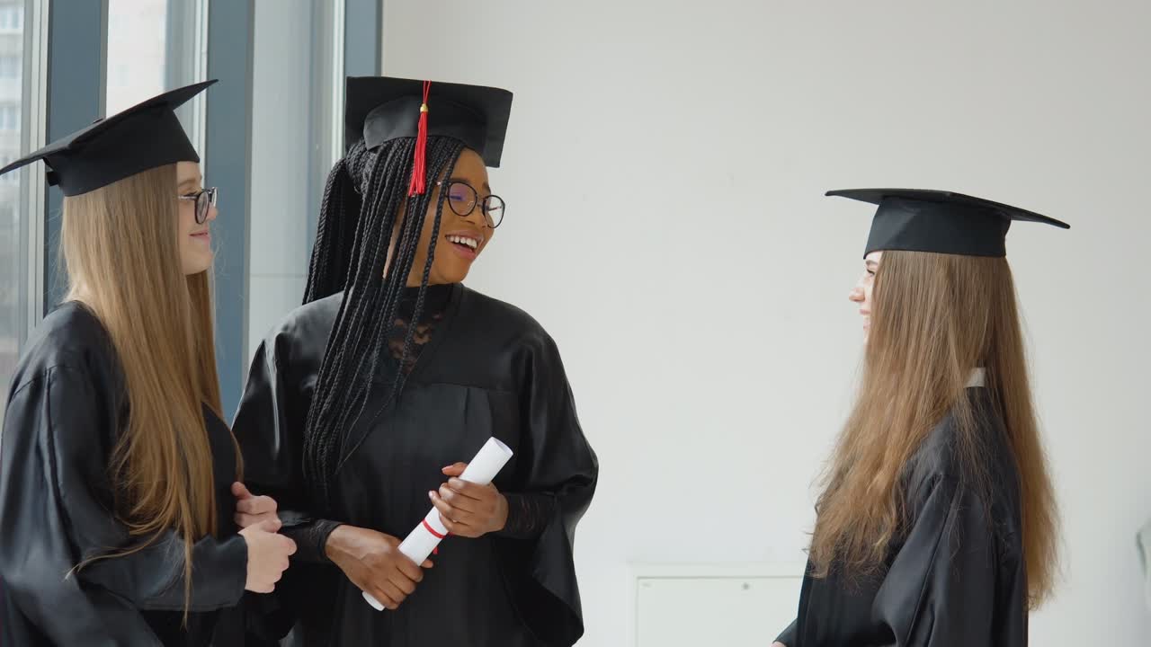 tres estudiantes femeninas de diferentes razas con un diploma en sus manos. graduados con túnicas negras y sombreros cuadrados tienen una conversación. concepto de educación