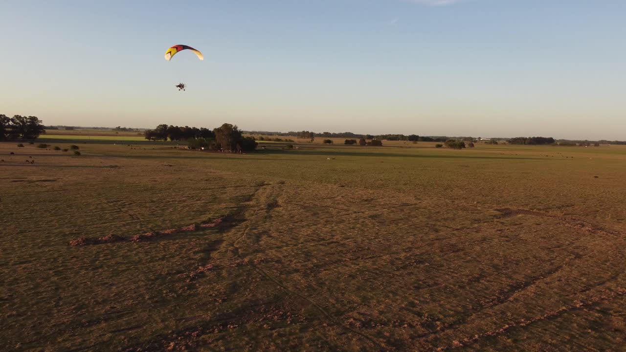toma aérea de parapente paratrike motorizado que vuela sobre el campo rural al atardecer dorado