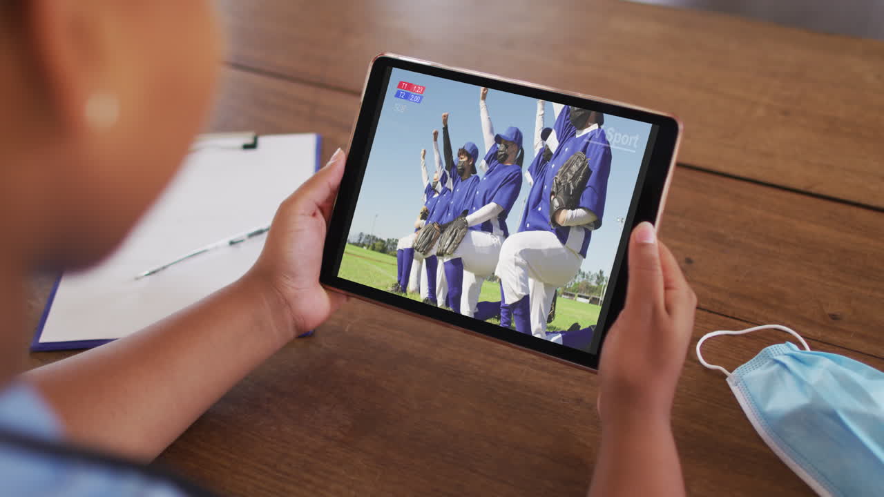 페이스 마스크를 쓰고 테이블에 앉아 코로나19 기간 동안 태블릿에서 야구를 보는 여성의 복합 사진