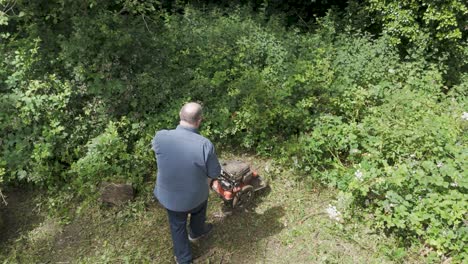 aerial view of a caucasian man using a mower to cut into heavily overgrown brambles in a rural area