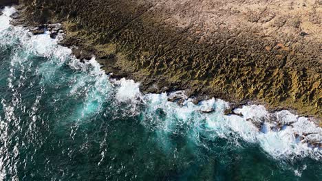 breccia rock formation tendrils from eroded water as waves crash on northside curacao shore, aerial