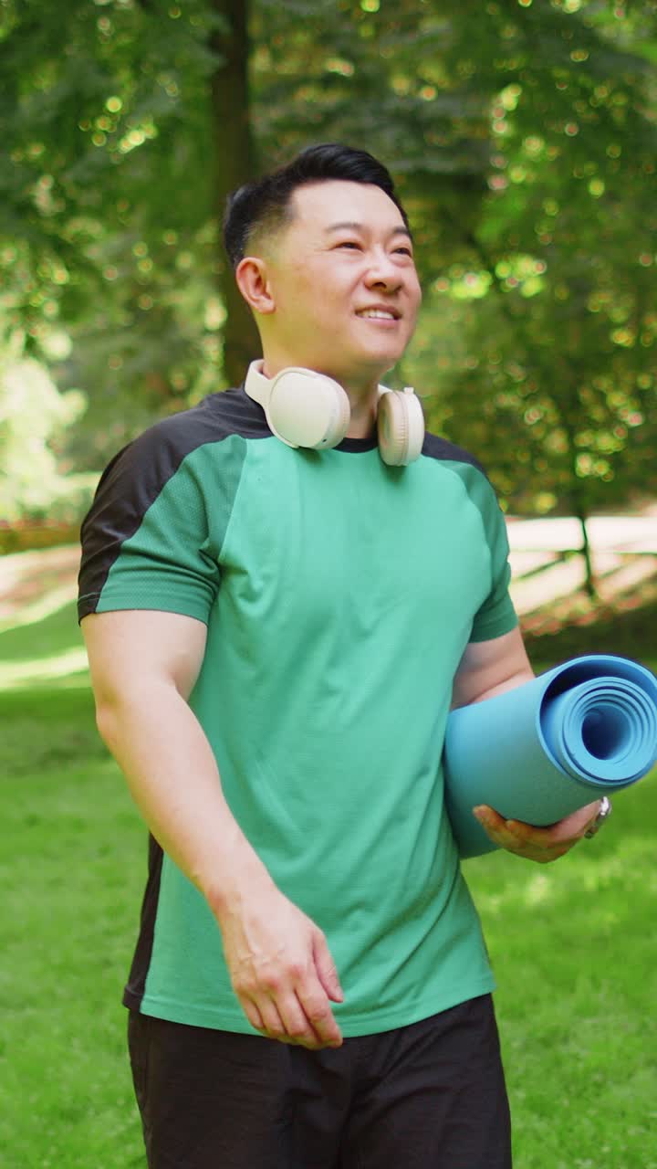 Athletic young man walking with rolled yoga mat to do fitness stretching workout exercises in park