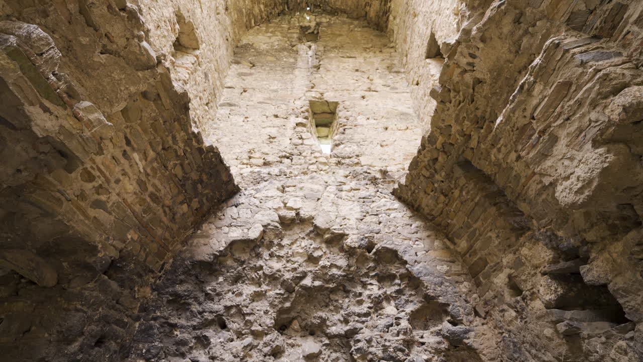 Low-to-high tilt inside Bukelon Fortress near Matochina, Bulgaria: rough masonry, vaulted arches and narrow slits forming a stark medieval chamber