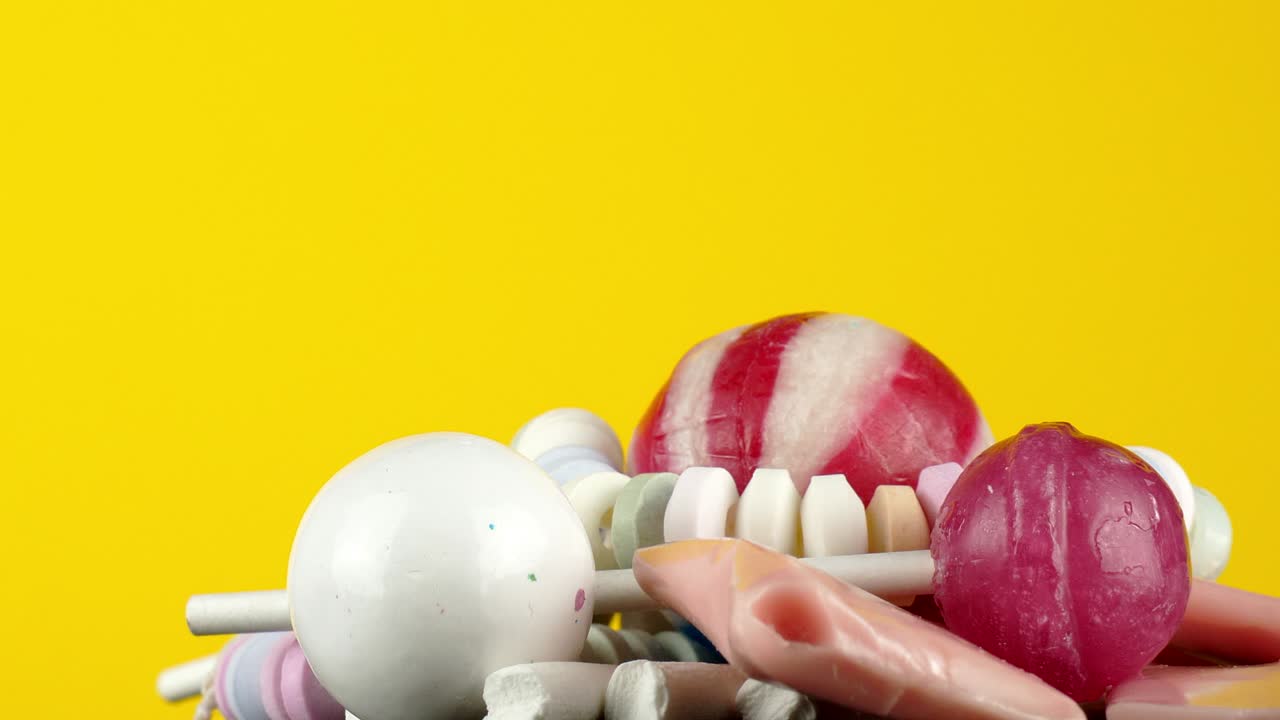 노란색 파스텔 배경에 회전하는 하드보일드 캔디 과자의 혼합물