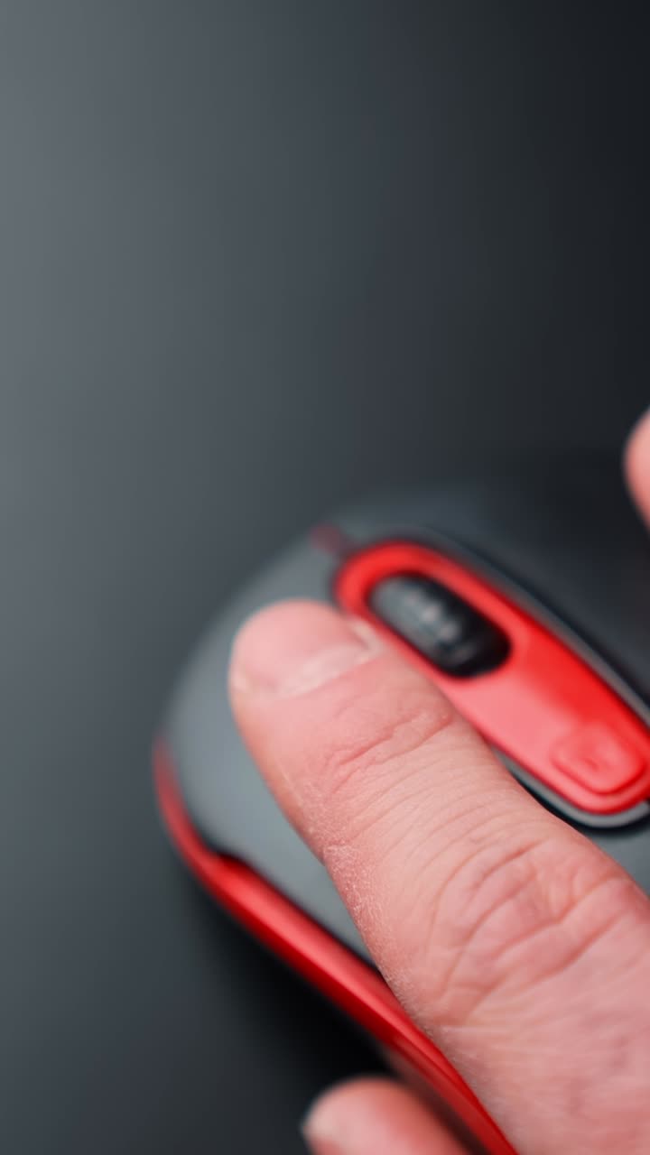 Vertical macro of a finger clicking a red and black computer mouse on a dark desk with copy space. Soft blur motion, quiet focused work vibe, minimal tech setup