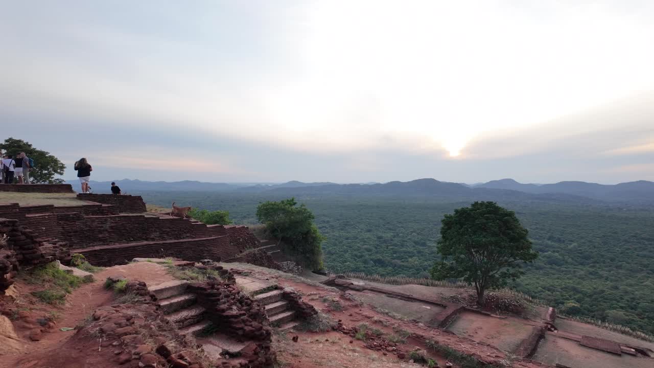 A tourist takes a photo of the serene sunrise from the top of Sigiriya Lion Rock, offering a breathtaking view over the lush landscape of Sri Lanka.