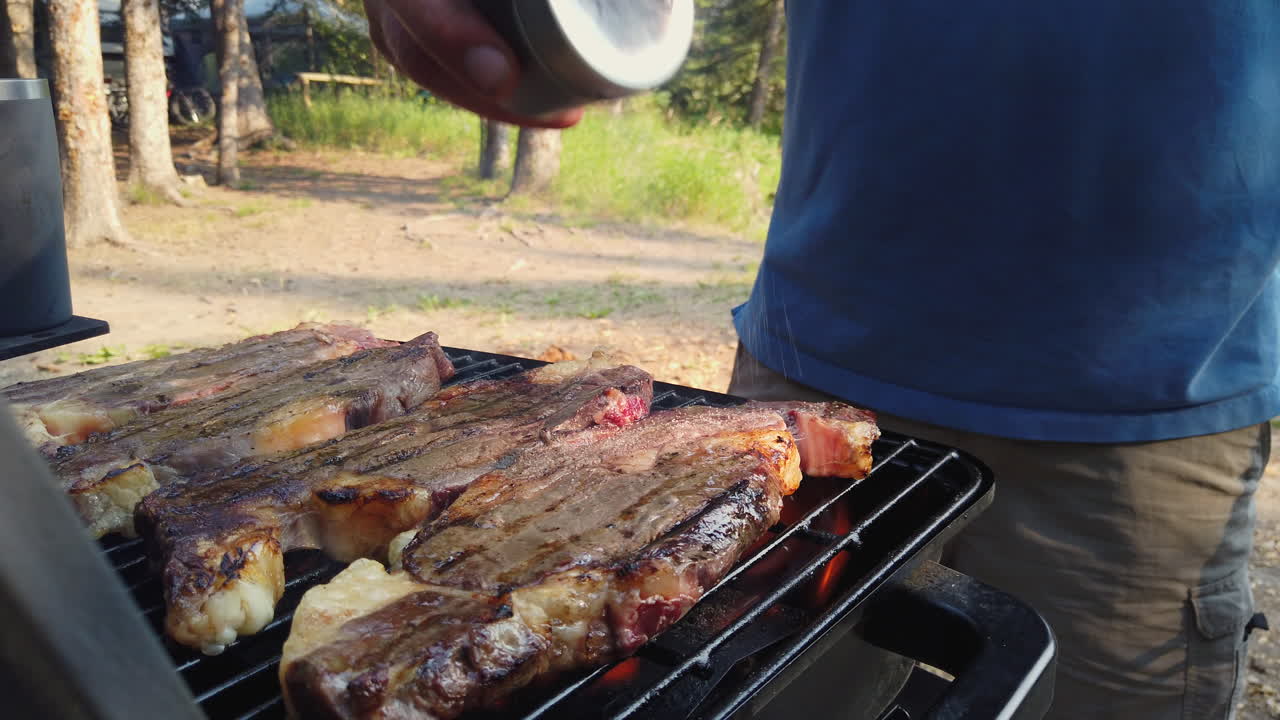 hombre adulto rociando sal y especias en bistecs a la parrilla en parrilla de barbacoa