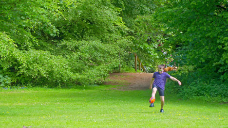 In-a-UK-summer-park,-a-boy-plays-and-walks,-while-others-enjoy-the-meandering-stream,-inviting-picnics,-and-Hubbard's-Hills'-woodland-charm