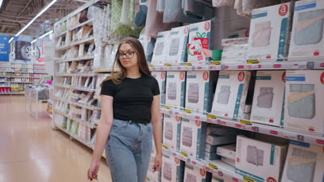 rear view of female shopper walking through mall aisle, carrying shopping bags while looking at products on the shelf, long hair flowing as she moves in a brightly lit retail environment