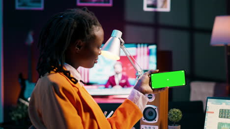 african american girl holds phone with isolated greenscreen at home,