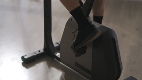 legs of elderly man on pedals of stationary bike indoors closeup view training at home healthy lifestyle sport activity in old age