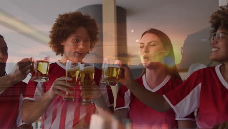 animation of sunset landscape over diverse friends in football shirts making toast in bar