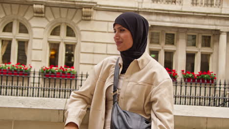 portrait of smiling muslim businesswoman wearing hijab and modern business suit standing and folding arms outside city office buildings 2