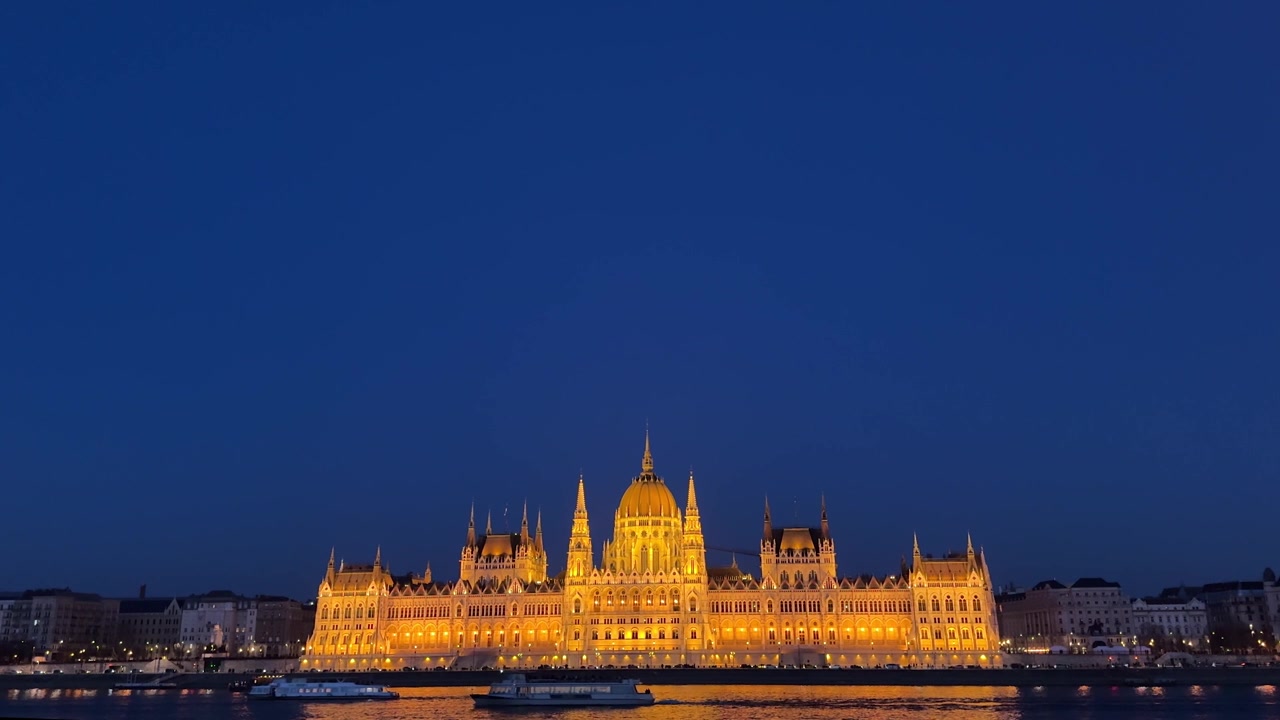 Ampia vista dell'iconico Országház di notte, barche che navigano sul fiume Danubio, Budapest
