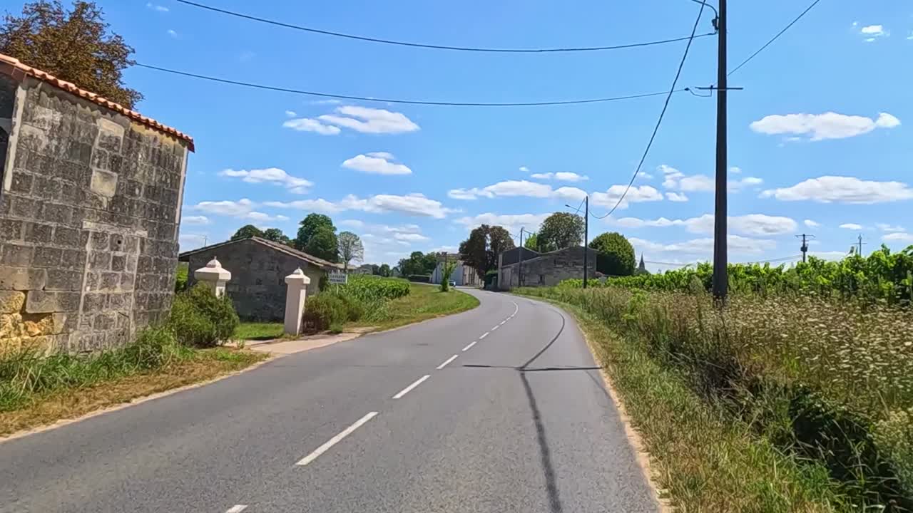 Experience a serene drive through lush vineyards and rustic stone buildings under a bright blue sky.