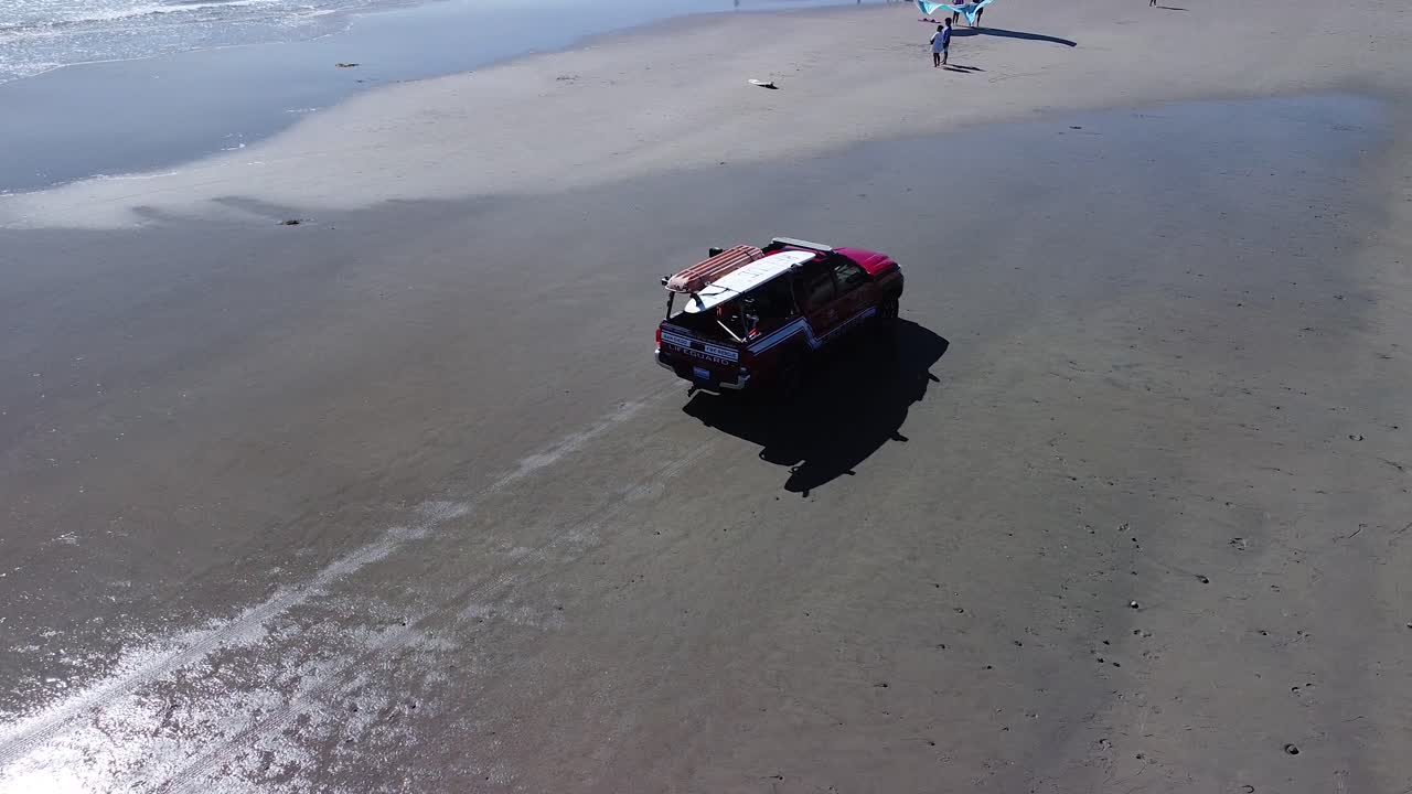 태평양 해변에서 빨간색 인명 구조원 트럭 주위를 돌고 있는 무인 항공기 보기