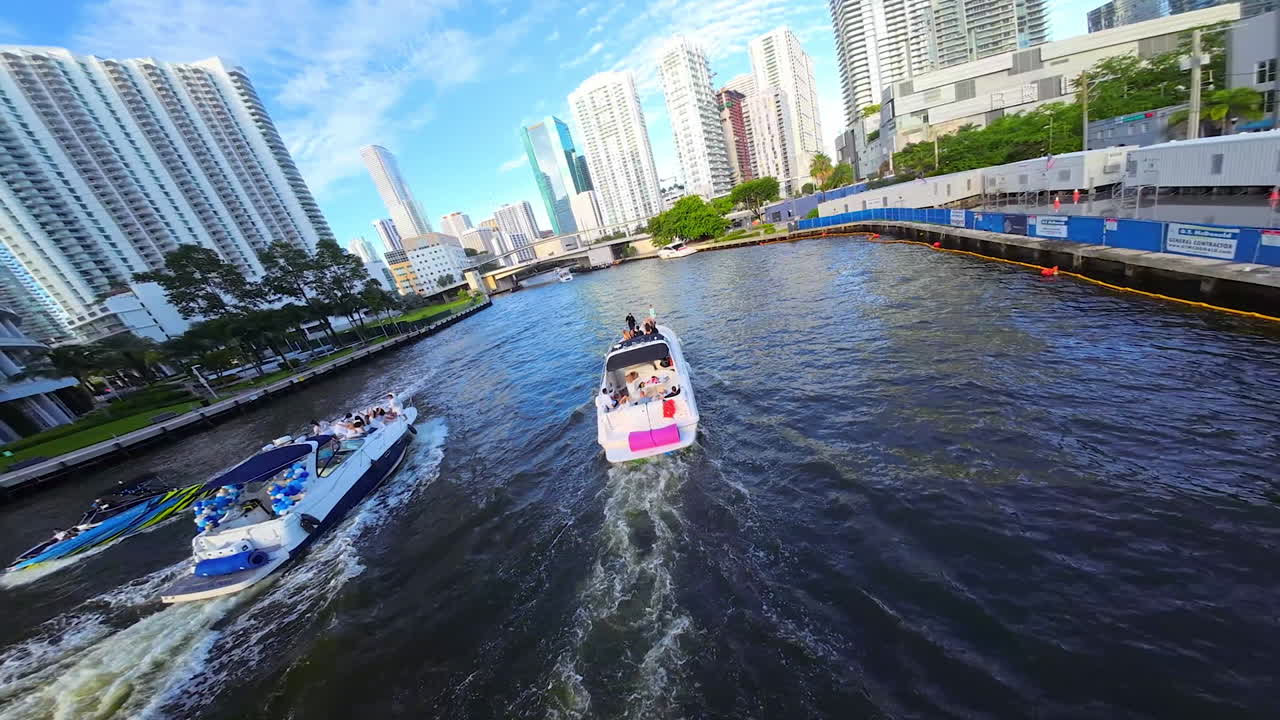 Several motor boats sail by the channel in modern American city. Footage from FPV drone above and around the vehicles.