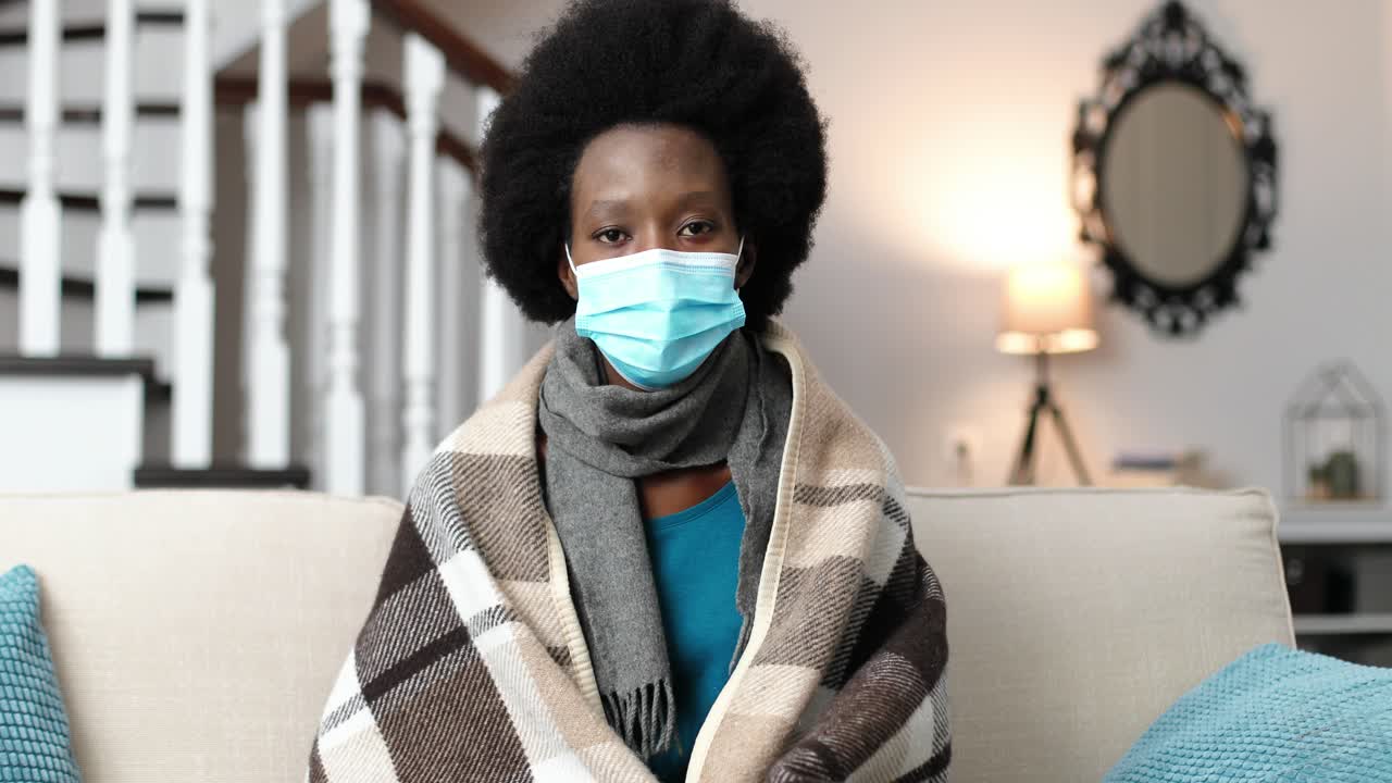 Close up portrait of African American female wearing a surgical mask ,sitting at home on sofa and looking at camera