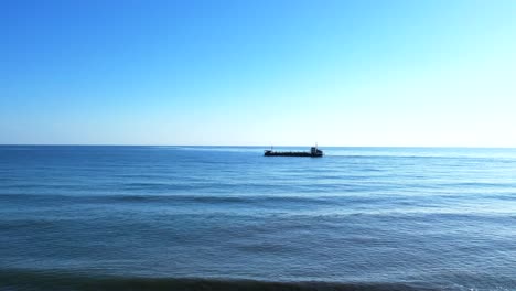 Vista-Aérea-Del-Barco-De-Carga-En-El-Mar,-Elevación-De-Drones-Desde-La-Playa-Mientras-Los-Niños-Juegan-En-La-Costa