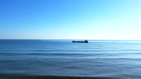 aerial view of freight ship in sea, drone lift from beach as kids playing at coast