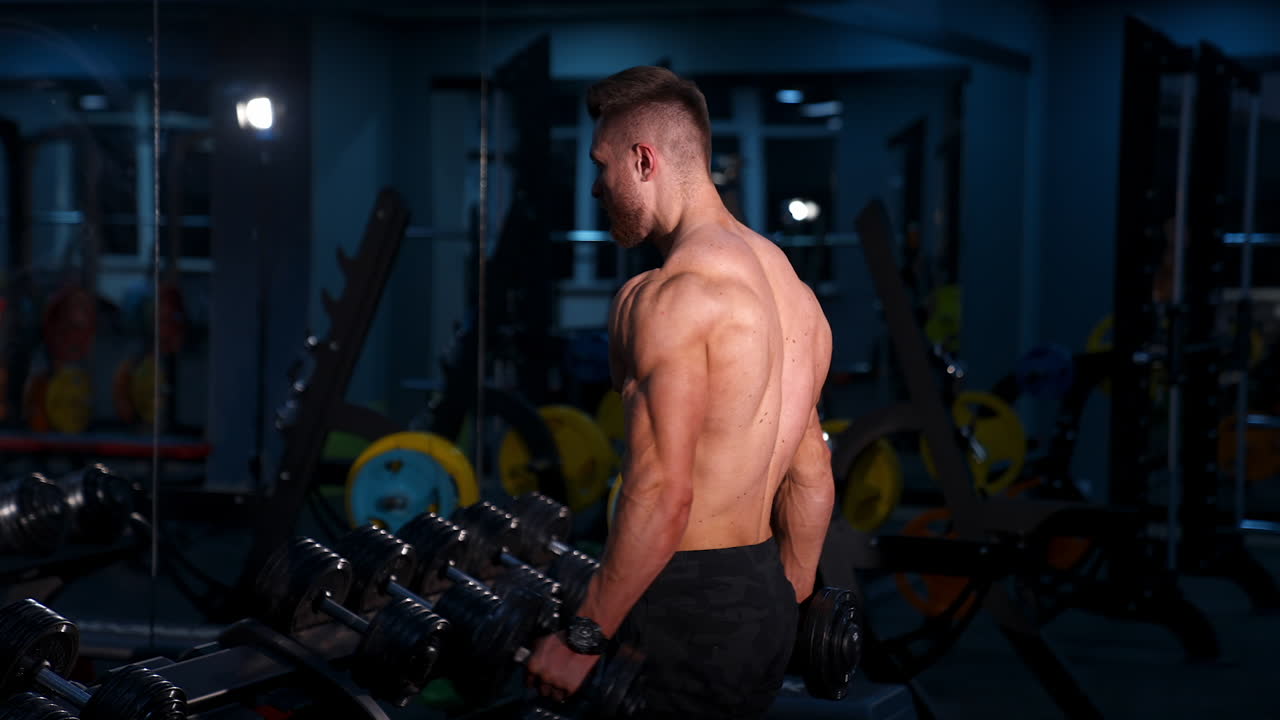 Fit young man lifting dumbbells doing workout at a gym. Sport, fitness, weightlifting, bodybuilding, training, athlete, workout exercises concept. View from the side.