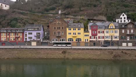 static shot of busses and cars going by typical old german houses along the moselle river in cochem, rhineland-palatinate