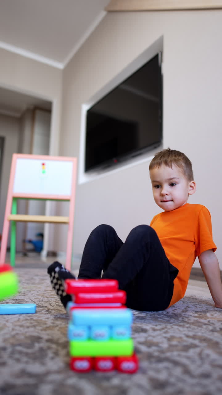 Caucasian toddler carefully puts blocks on the pile. Adult helps the kid to build a tower. Vertical video.