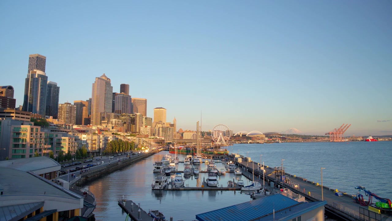 Ampia vista dal ponte panoramico sul tetto del Bell Street Pier di Seattle che mostra il centro città, un porto turistico pieno di barche e il lungomare, con la Great Wheel, gli stadi e il Monte Rainier in lontananza, Inquadratura statica