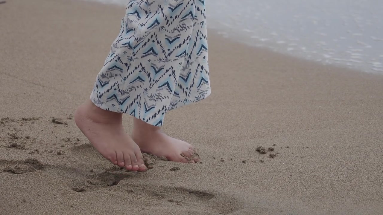 Persona a piedi nudi in piedi su una spiaggia sabbiosa vicino alle onde dell'oceano