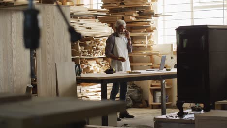 african american male carpenter talking on smartphone in a carpentry shop