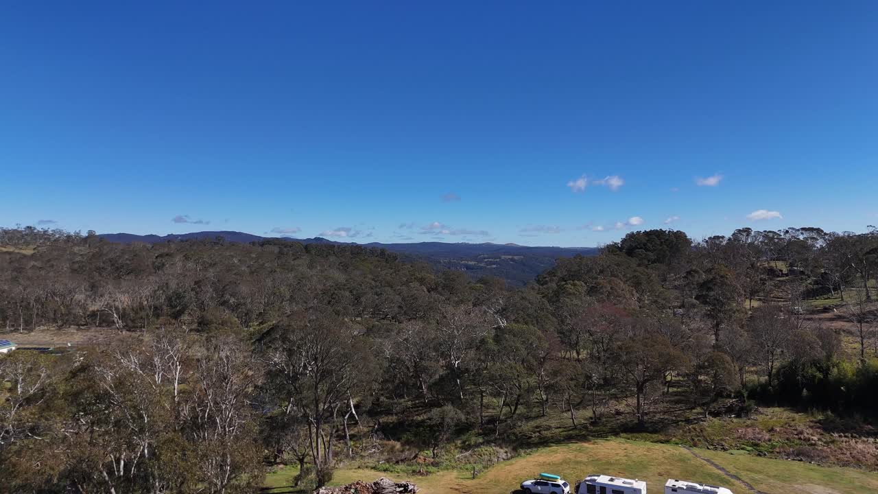 Drone footage begins above a roadside motel, gradually panning to reveal expansive bushland and rolling hills under clear midday sunlight in rural Australia