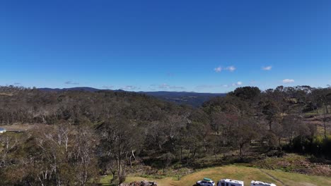drone footage begins above a roadside motel, gradually panning to reveal expansive bushland and rolling hills under clear midday sunlight in rural australia