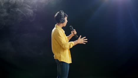 vista lateral de un joven asiático con auriculares sosteniendo un micrófono y cantando sobre el fondo blanco de humo negro