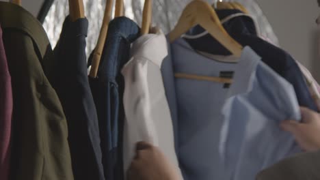 young man at home choosing business suit from clothes rail for job interview 1