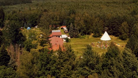 Antena-De-Drones-Volando-Sobre-Un-Bosque-Verde-Denso-Que-Revela-Un-Centro-De-Eventos-épico-Con-Un-Tipi-Masivo-Y-Una-Clase-De-Yoga-Al-Aire-Libre-Que-Tiene-Lugar