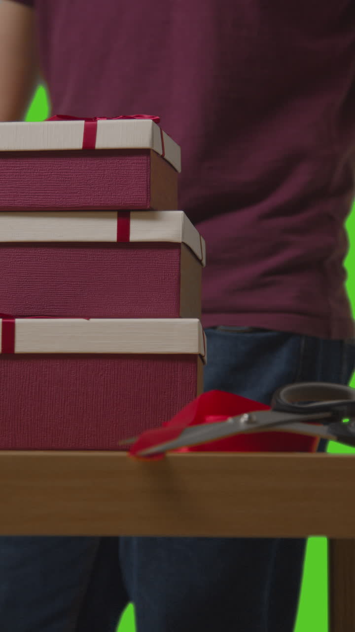 video vertical de un hombre recogiendo pilas de regalos en cajas envueltas en regalos de la mesa disparado contra la pantalla verde 2