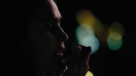 hermosa joven aplicando maquillaje de lápiz labial en la ciudad por la noche preparándose para una fiesta nocturna con luces bokeh en el fondo