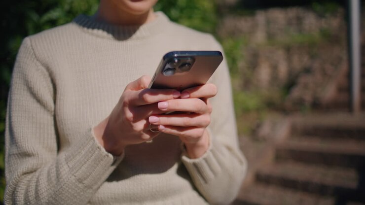 Primo piano di una ragazza che cammina in un parco soleggiato mentre scrive un messaggio al cellulare. Donna che digita sullo schermo