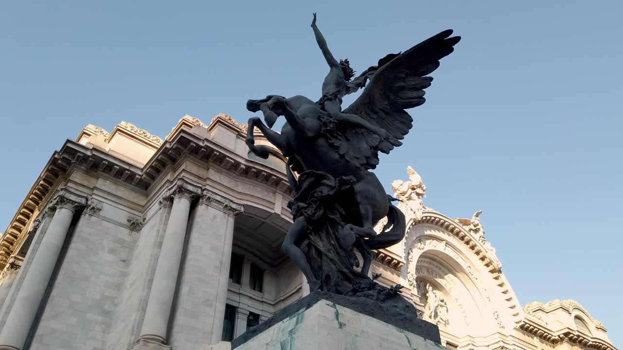 Pan right revealing a dramatic bronze sculpture and historic building facade under clear daylight