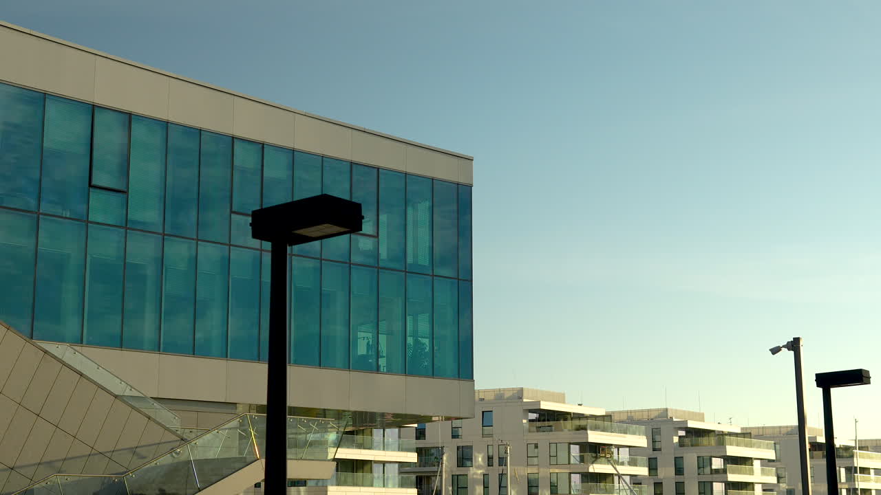 edificio de vidrio moderno con reflejo del cielo azul, lámparas de calle en un entorno urbano al anochecer