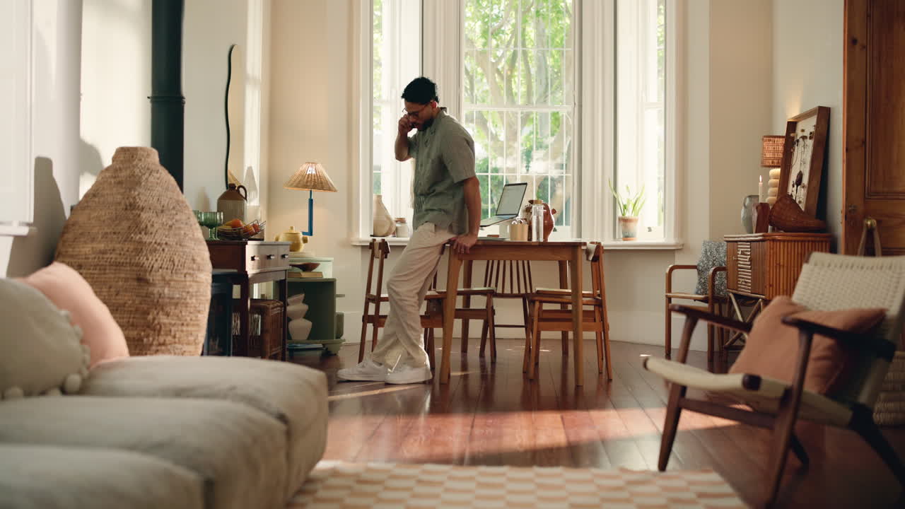 Man Talking on Phone While Leaning on Table in Bright Home