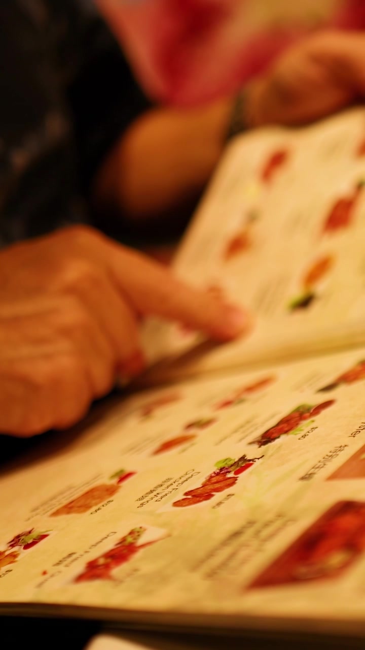 En person kigger på en farverig menu i varmt, dæmpet lys, hvilket skaber en afslappet spiseatmosfære.