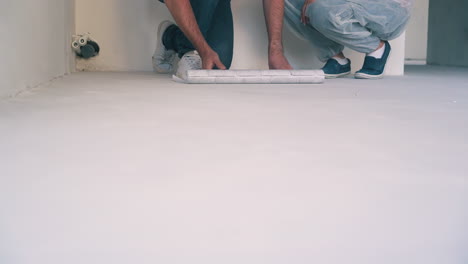 couple unrolls wallpaper on floor in light room closeup