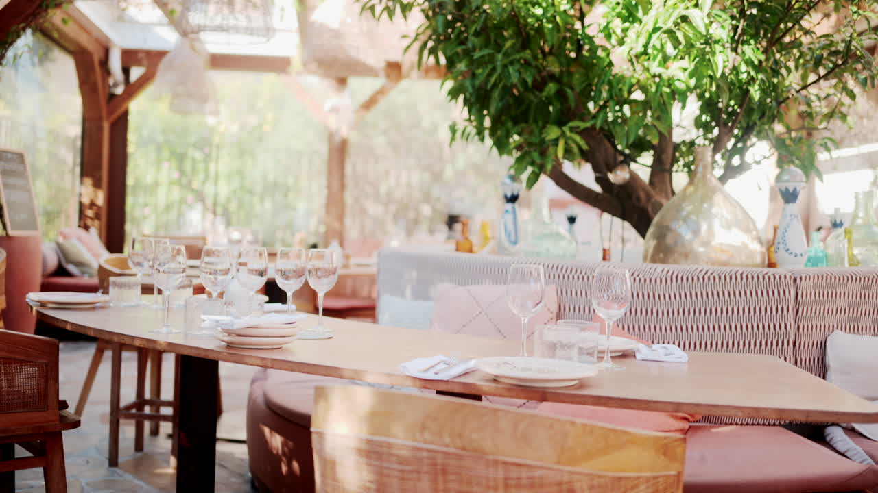 Wooden restaurant table prepared with glasses, plates, and napkins in warm natural light