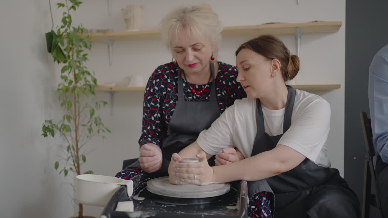 A female master shares her skills while giving a lesson for the elderly. Show grandmother the technique of working on a potter's wheel with ceramic clay
